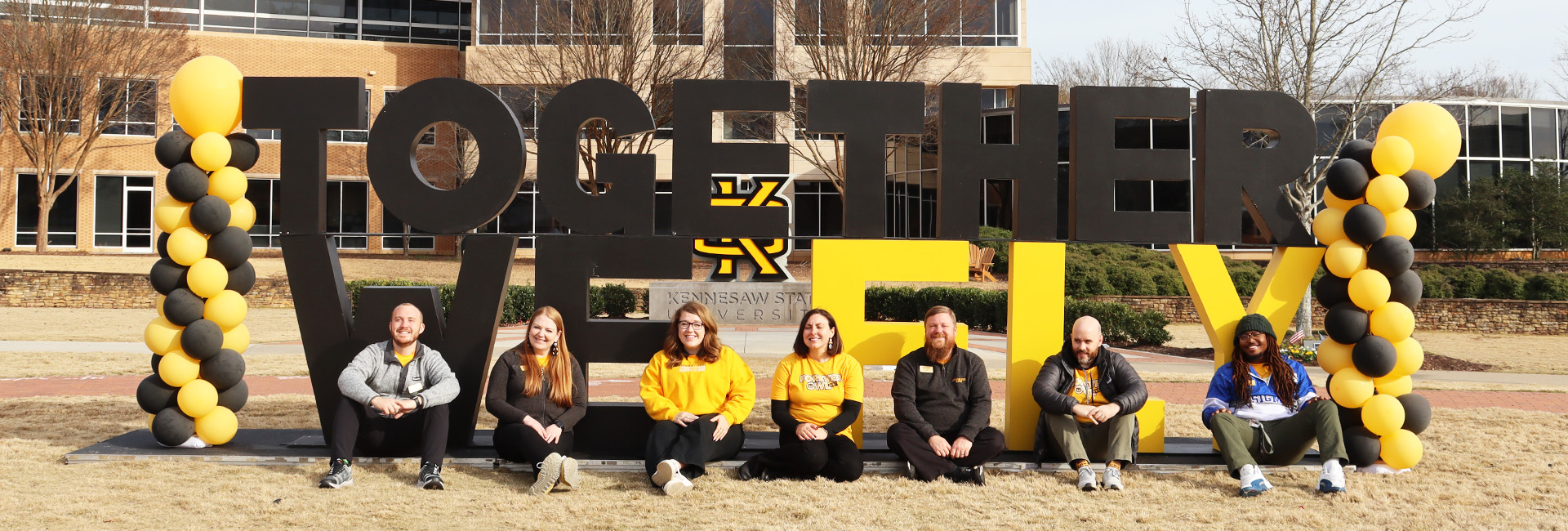 Alumni team seated in front of together we fly sign