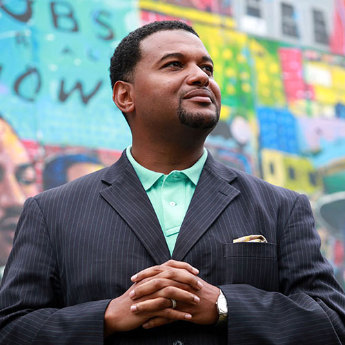 Nathaniel Smith posing in a suite, with his fingers intertwined.