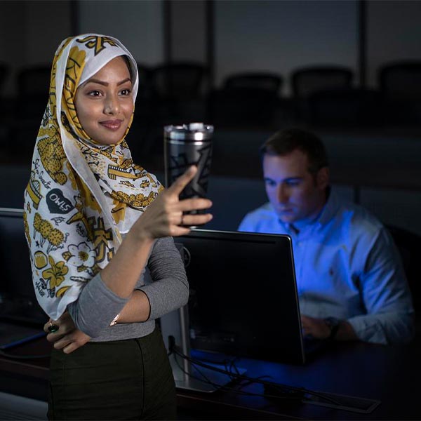 ksu student smiling for picture while a student in the background is using a laptop.