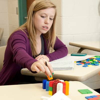 A student working with colorful interlocking cubes at a math classroom desk.