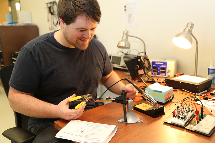 Student working on an electronic project at a desk with tools and components in a physics laboratory