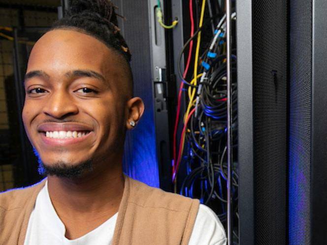 Man smiling for picture with eletrical panel wires coming out of it behind him