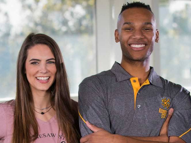 Two students standing infront of a window smiling for a picture