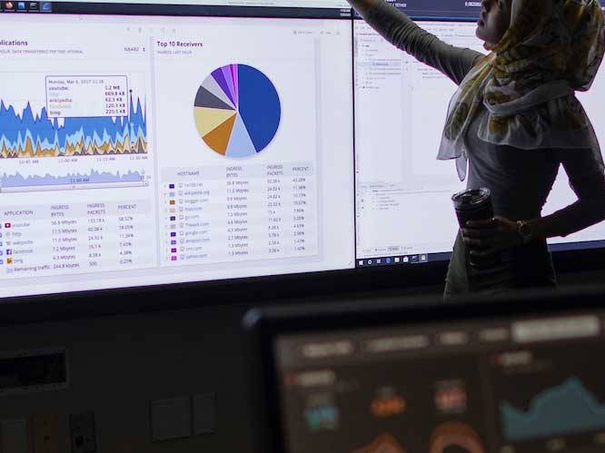 Woman infront of projector pointing to colorful graphs on screen