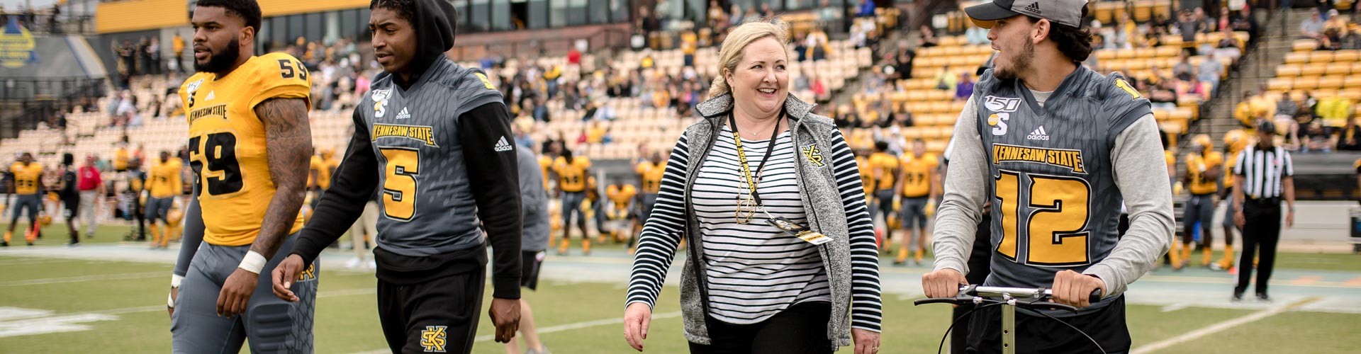 KSU's homecoming game with 2 players and 2 KSU Staff members walking on the field