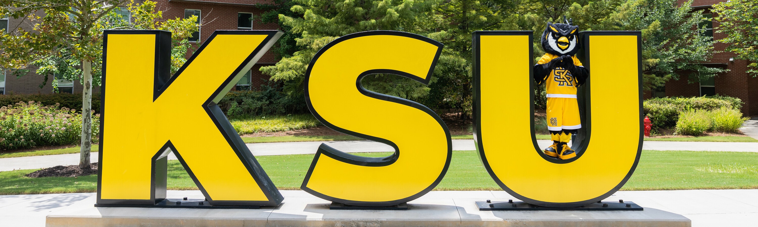 Scrappy standing inside of KSU letters on campus