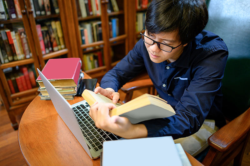 Student looking up research resources at a desk and reading